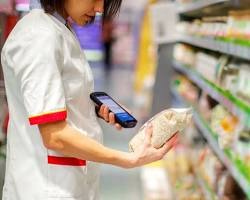 A shopper in a store aisle holding a bag of food and scanning it with a handheld scanner